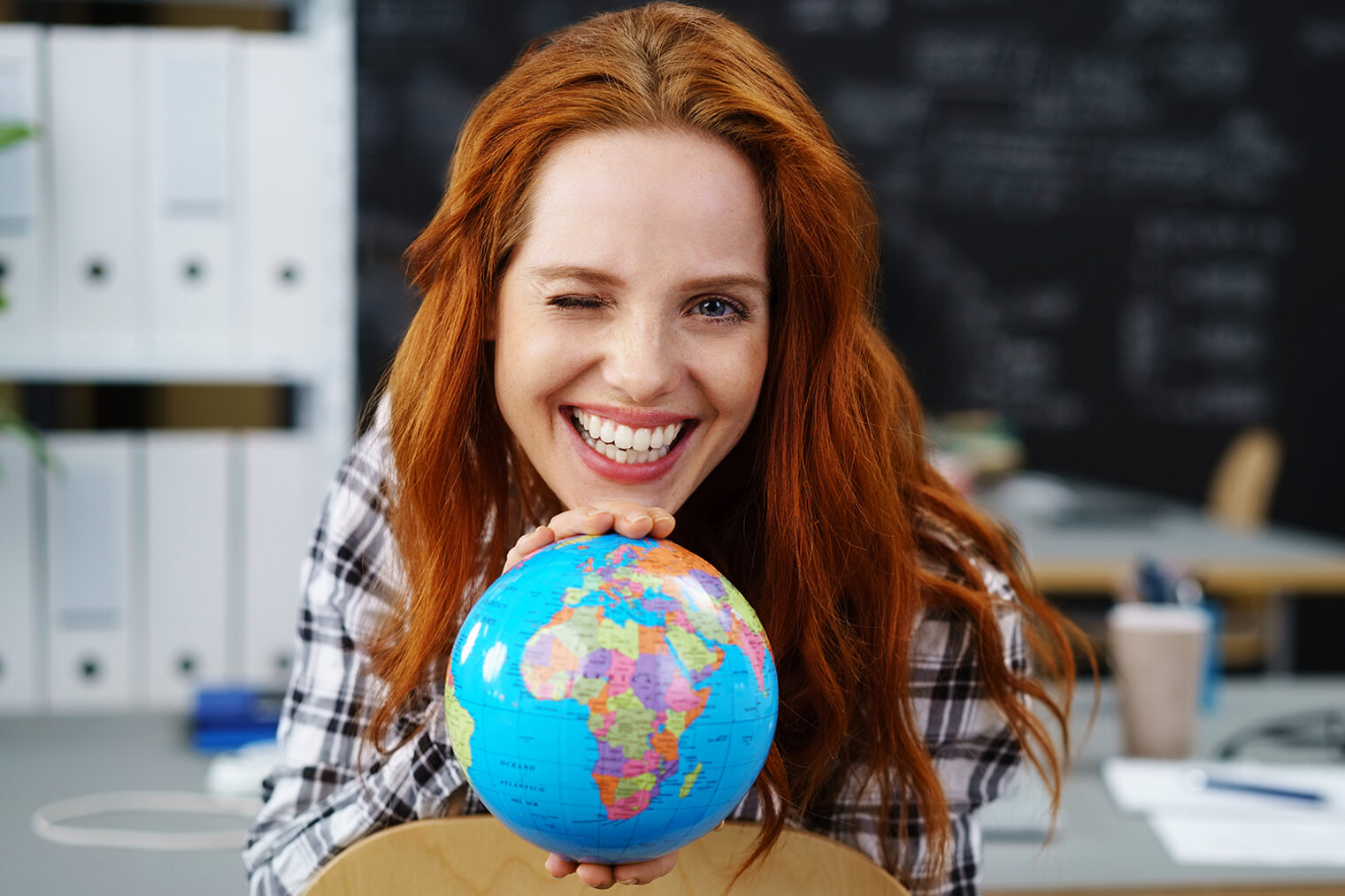 frau zeigt einen globus und zwinkert mit einem auge